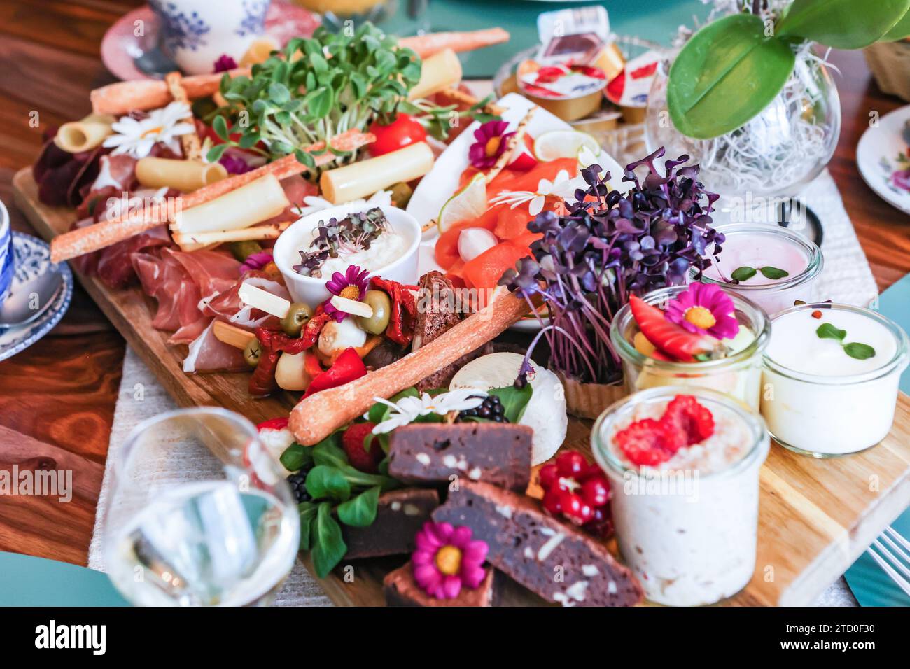 Una vivace tavola di salumi gourmet piena di un assortimento di formaggi, carni e fiori commestibili. Foto Stock