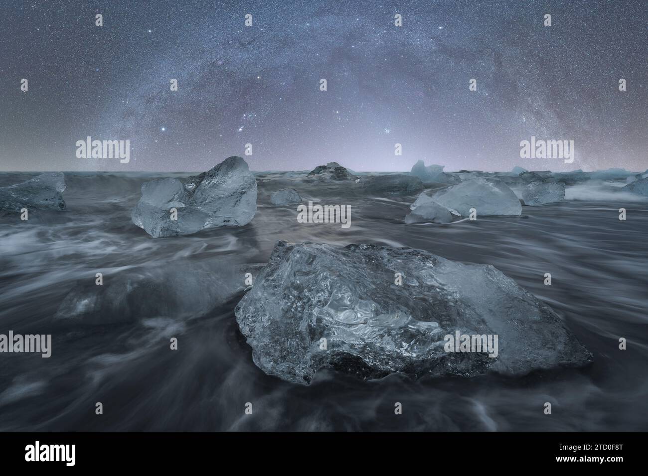 Le formazioni di ghiaccio brillano sotto un cielo stellato, con onde dolci che le circondano sulle rive di Diamond Beach, Islanda Foto Stock