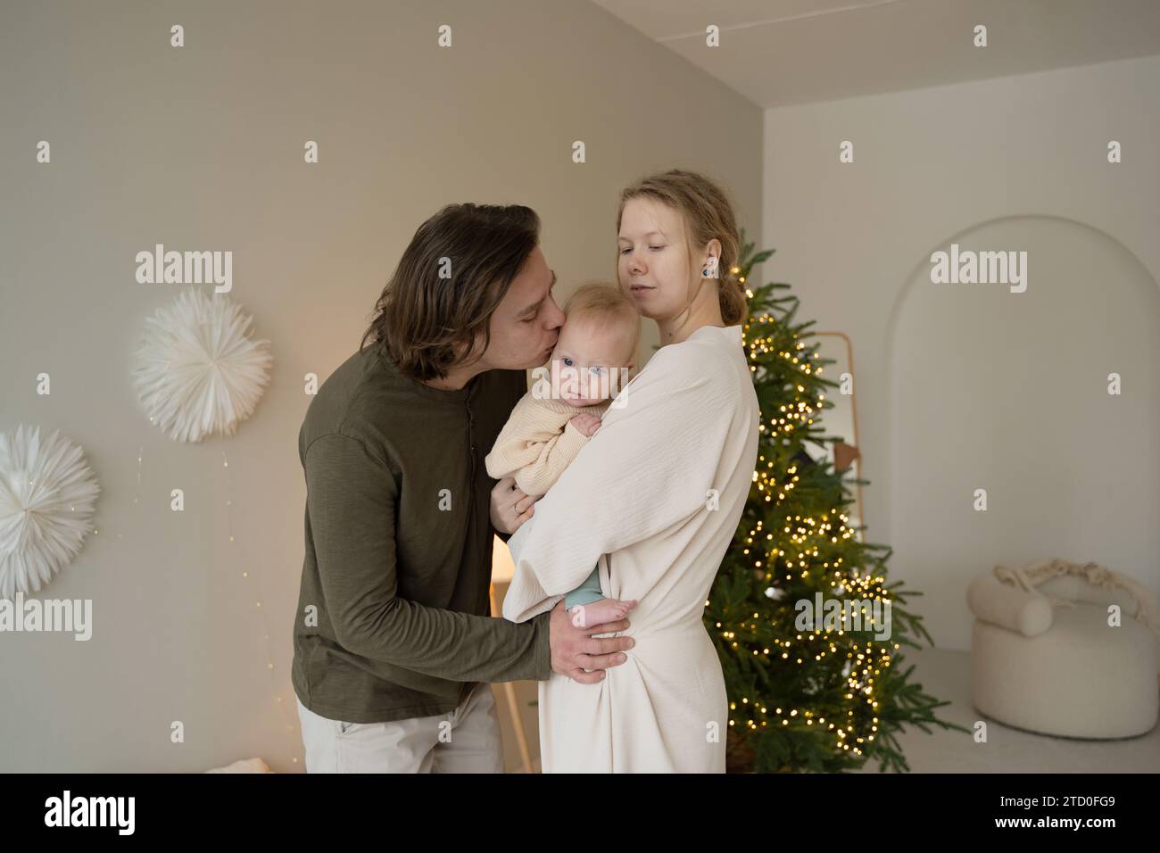 Una famiglia amorevole condivide un momento di tenerezza con il bambino vicino a un albero di Natale adornato di luci. Foto Stock
