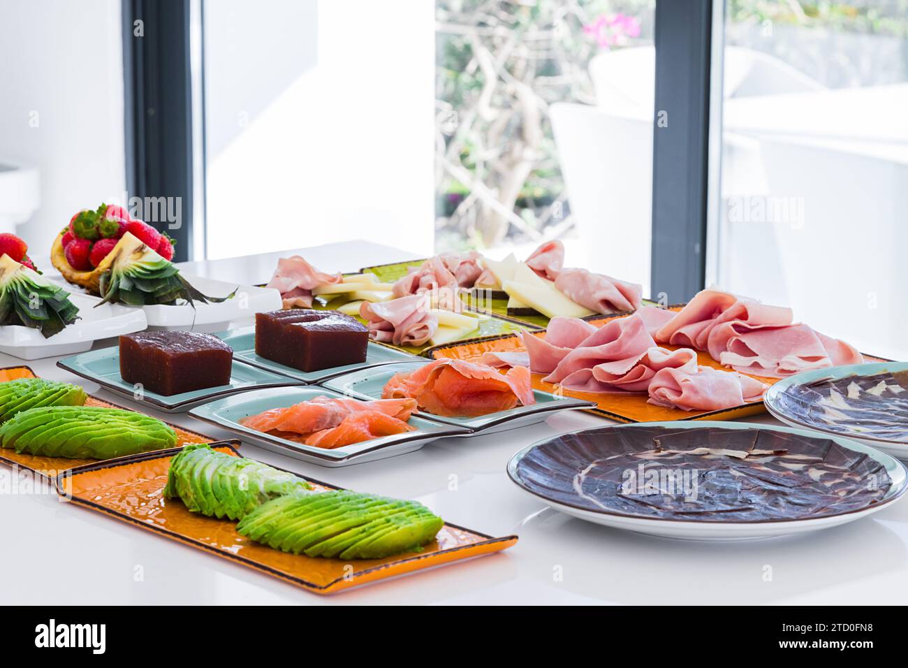 Alto angolo di appetitoso affettato di avocado salmone e prosciutto servito su piatti vicino al dessert e frutti di bosco messi sul bancone in una cucina leggera Foto Stock