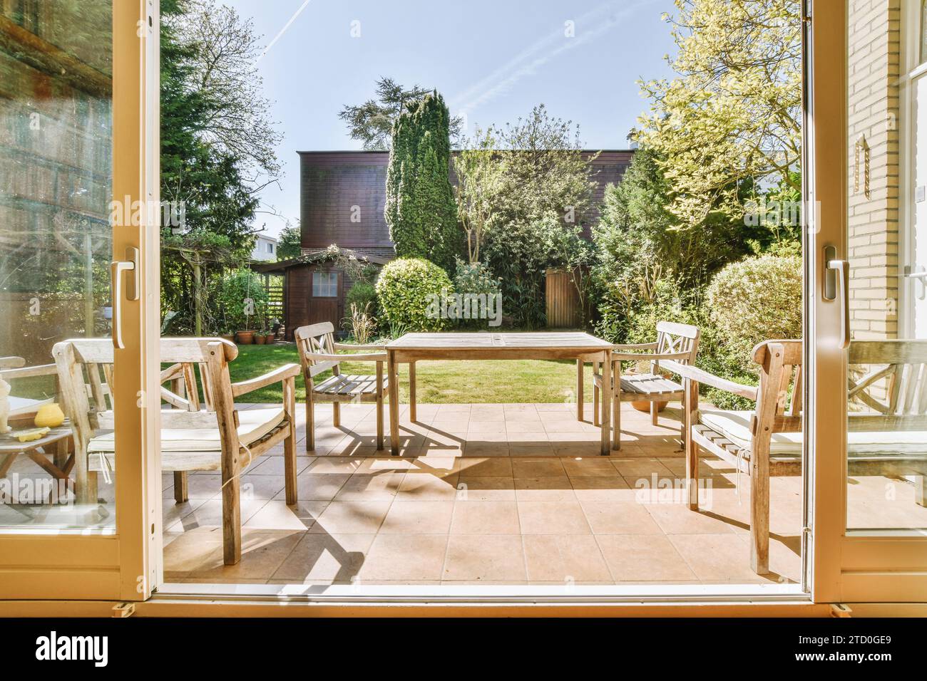 Tavolo da pranzo e sedie in legno su pavimento piastrellato di un moderno patio di casa con giardino sullo sfondo Foto Stock