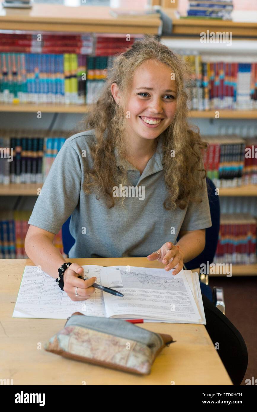 Una donna studentessa di livello si siede a una scrivania in una biblioteca scolastica in revisione. Foto Stock