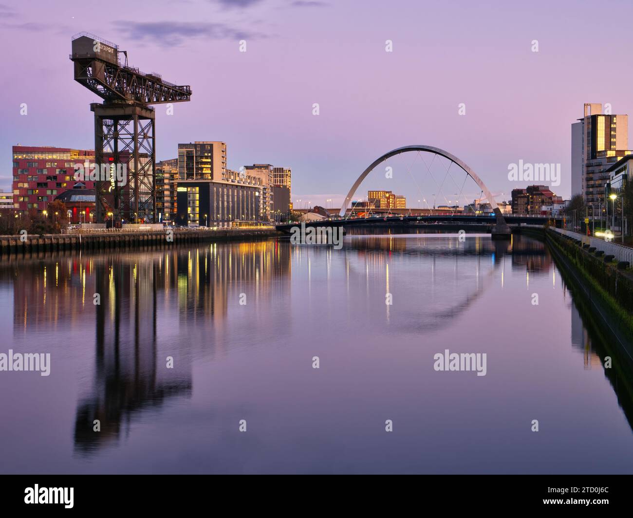 La serata si avvicina al fiume Clyde a Glasgow, con la città illuminata in lontananza e lo Squinty Bridge e la gru Finnieston Foto Stock