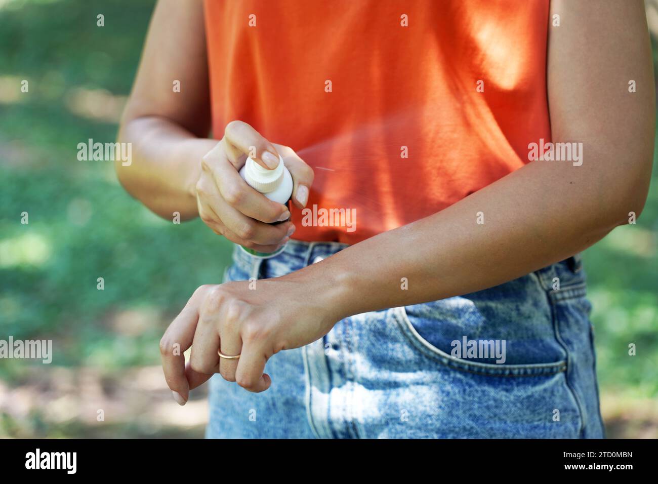 Ragazza che spruzza repellente per insetti sul braccio all'aperto in natura utilizzando un flacone spray. Repellente per zanzare. Spray anti insetti. Foto Stock