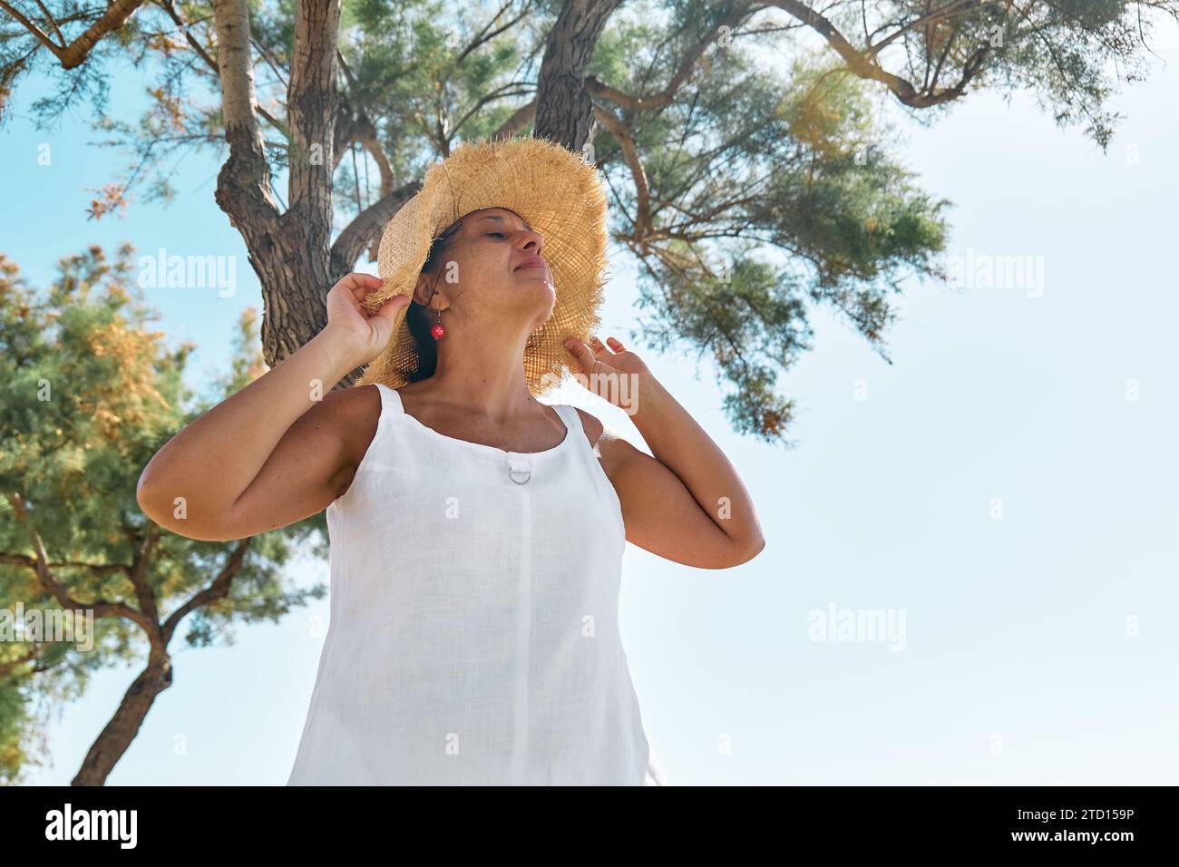 Attraente donna sorridente di mezza età che indossa un cappello di paglia al mare. Donna matura felice che gode della libertà in mare e guarda lontano dal cielo. Foto Stock
