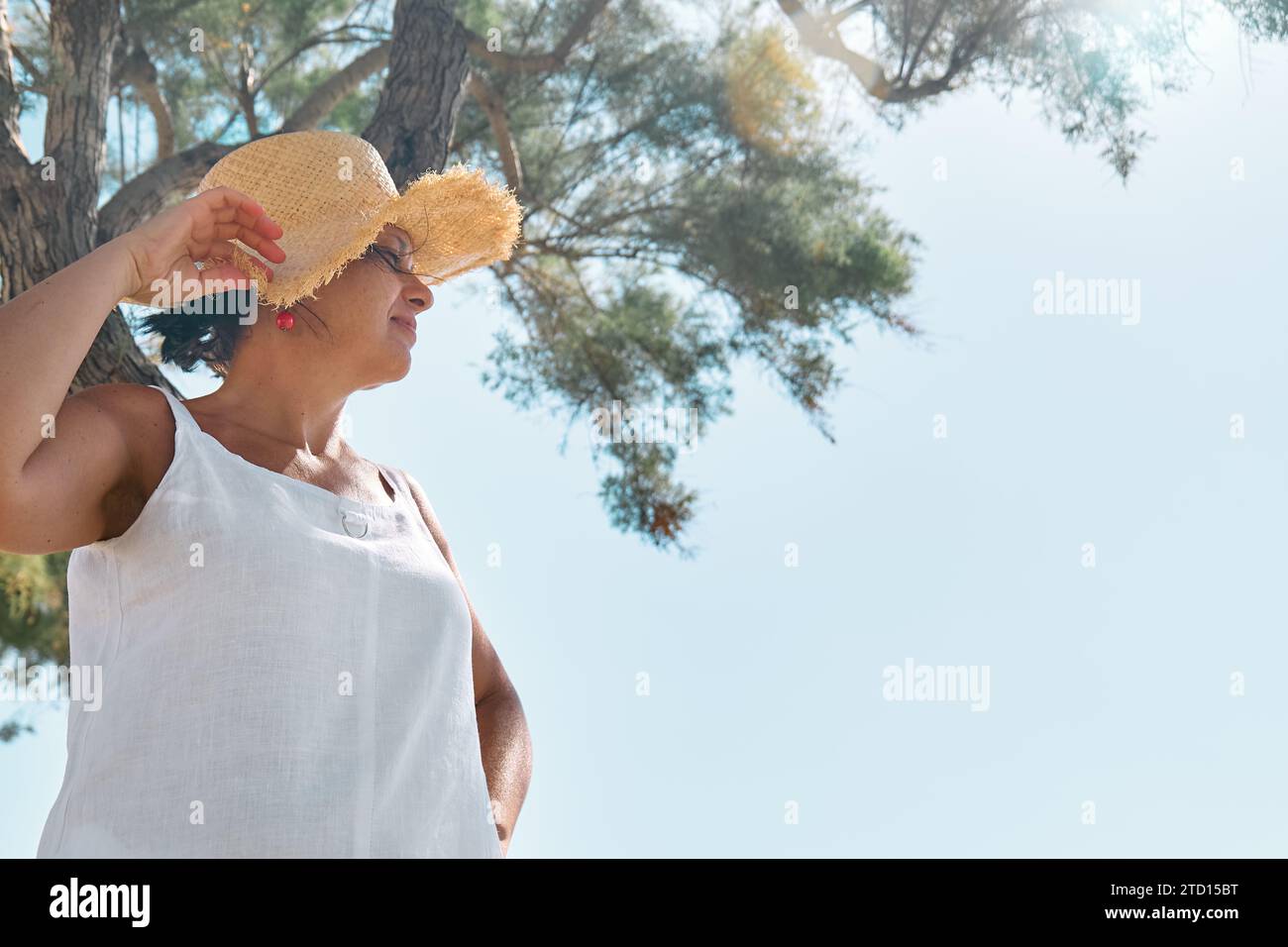 Attraente donna sorridente di mezza età che indossa un cappello di paglia al mare. Donna matura felice che gode della libertà in mare e guarda lontano dal cielo. Foto Stock