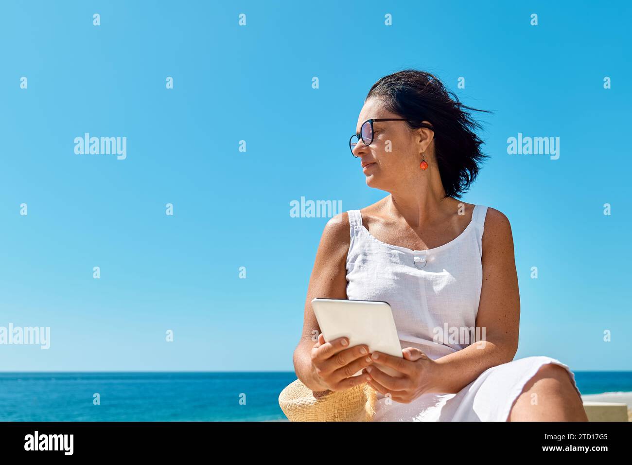Donna matura che indossa un tablet digitale in spiaggia. Donna di mezza età che utilizza un dispositivo digitale per lo shopping online, bancario, sui social media o per la lettura Foto Stock