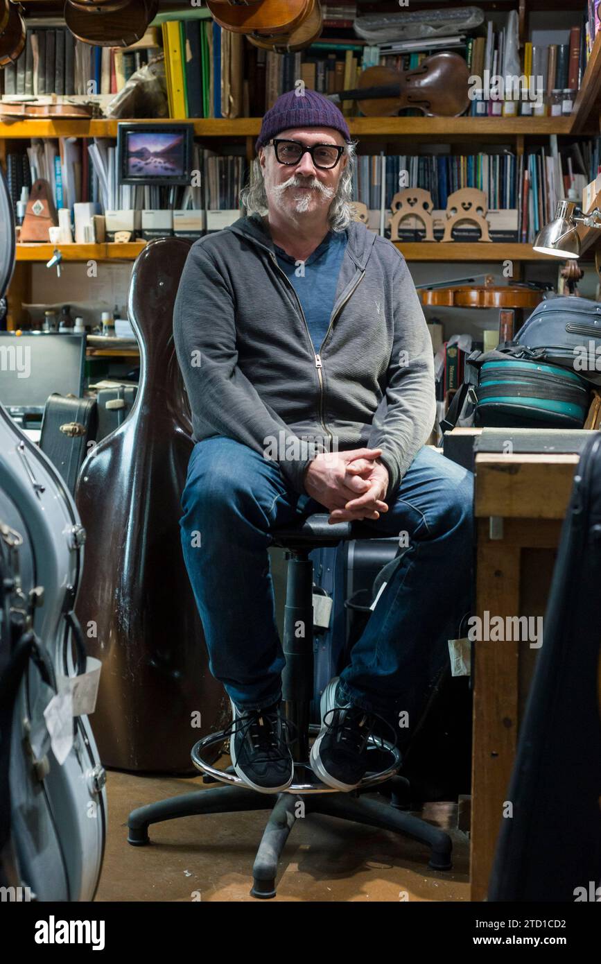 Un esperto restauratore di strumenti musicali ad arco siede nel suo laboratorio a Londra. Foto Stock
