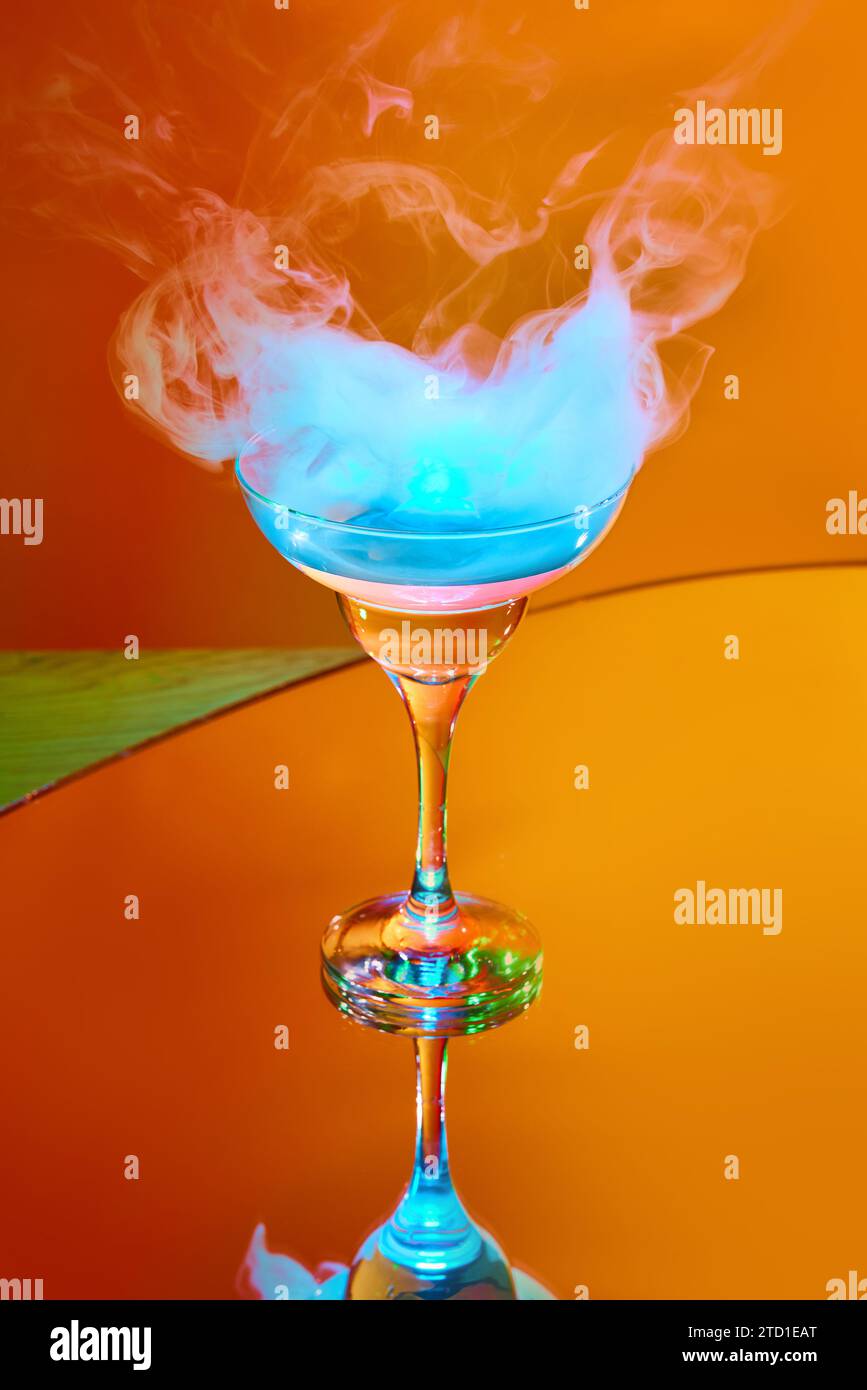 Servizio di bevande stravaganti. Bicchiere con cocktail martini e fumo sulla parte superiore su sfondo arancione con luce al neon Foto Stock