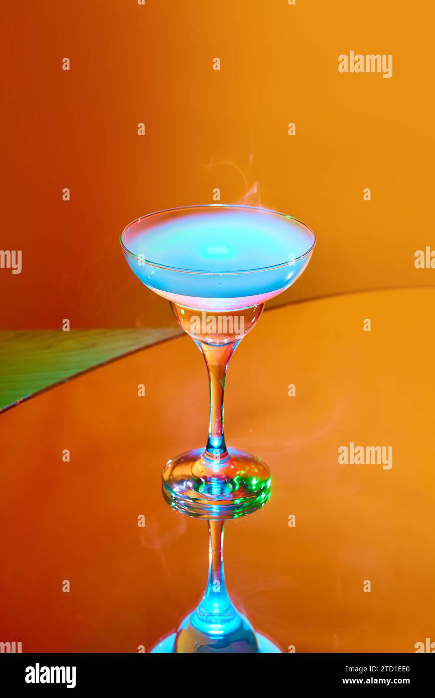 Servizio di bevande stravaganti. Bicchiere con cocktail martini e fumo sulla parte superiore su sfondo arancione con luce al neon Foto Stock