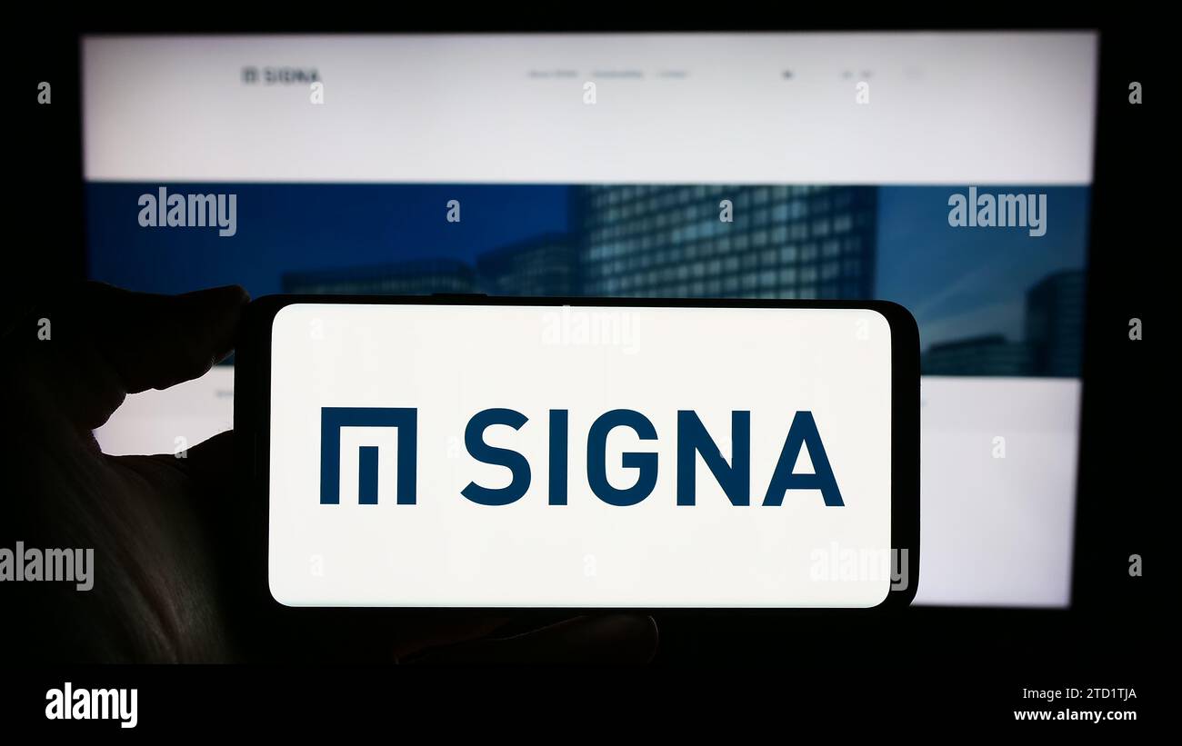 Persona in possesso di un cellulare con il logo della società immobiliare austriaca Signa Holding GmbH davanti alla pagina web aziendale. Concentrarsi sul display del telefono. Foto Stock