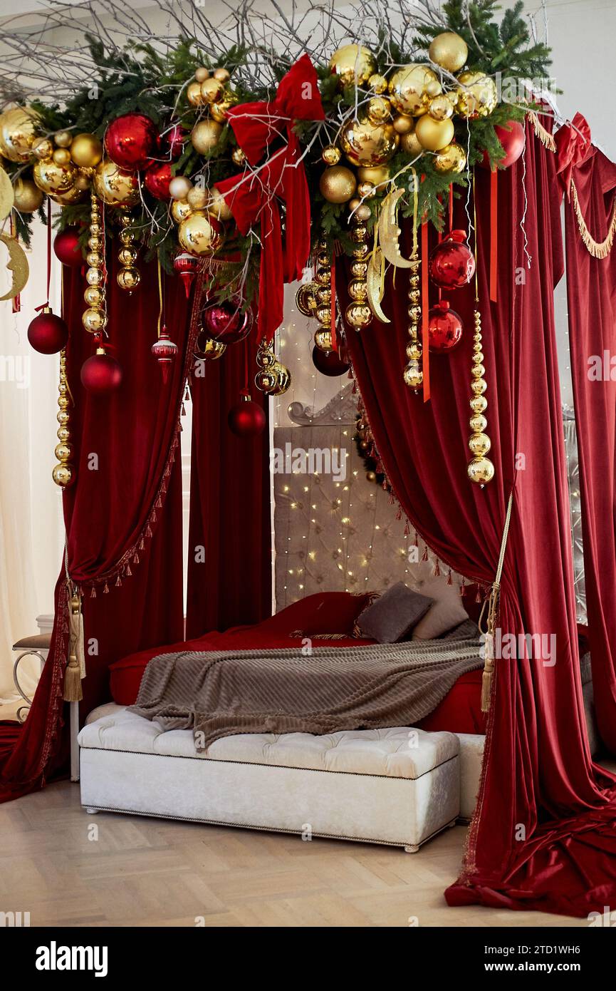 Un letto rosso con un alto baldacchino di velluto, con balli di Natale e decorazioni Foto Stock