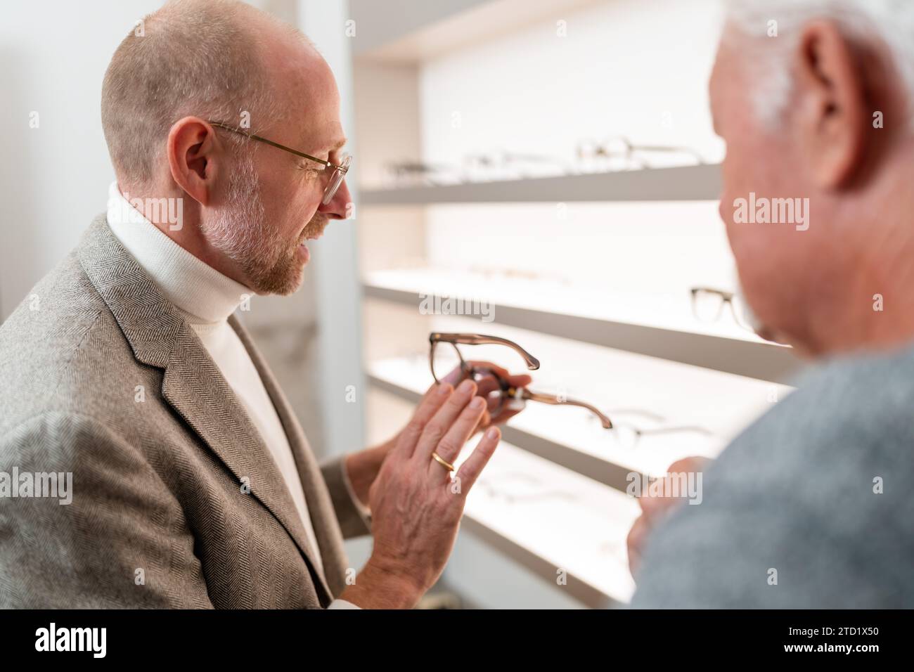 Un'ottica che mostra e spiega nuovi occhiali al cliente in un negozio luminoso Foto Stock