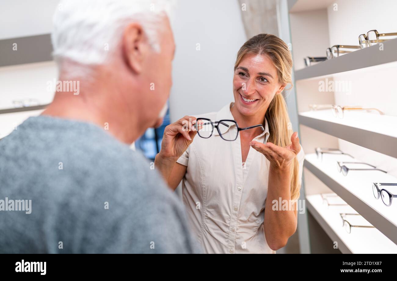 Un'ottica che assiste un cliente senior nelle scelte di occhiali. donna sorridente che mostra occhiali in negozio. Foto Stock