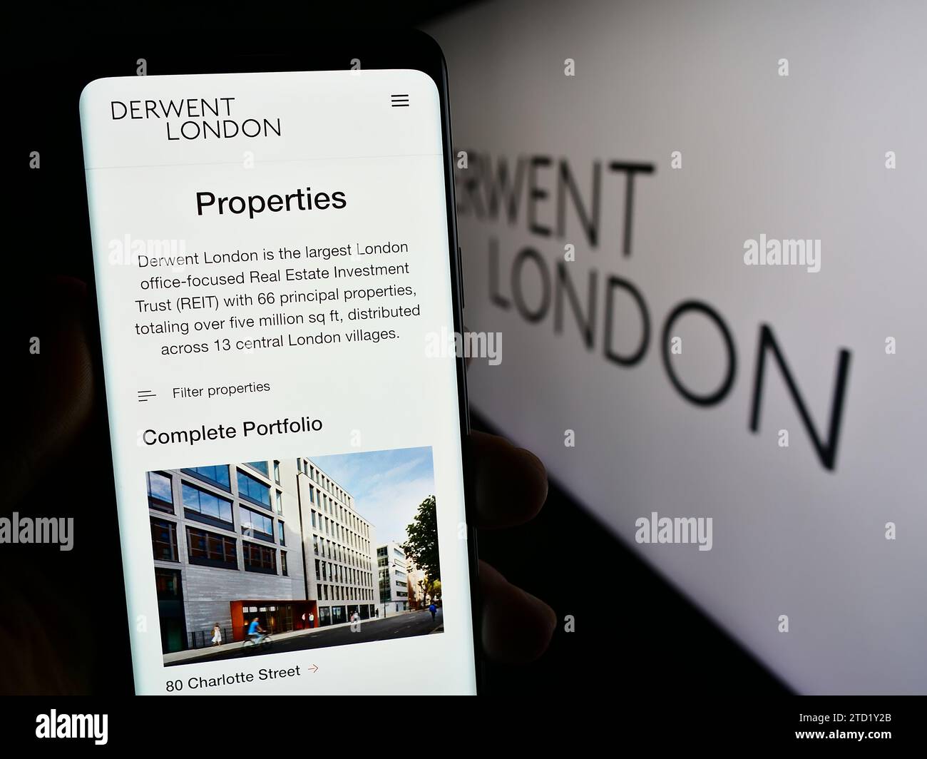 Persona che possiede uno smartphone con una pagina Web della società immobiliare britannica Derwent London plc davanti al logo. Concentrarsi sul centro del display del telefono. Foto Stock