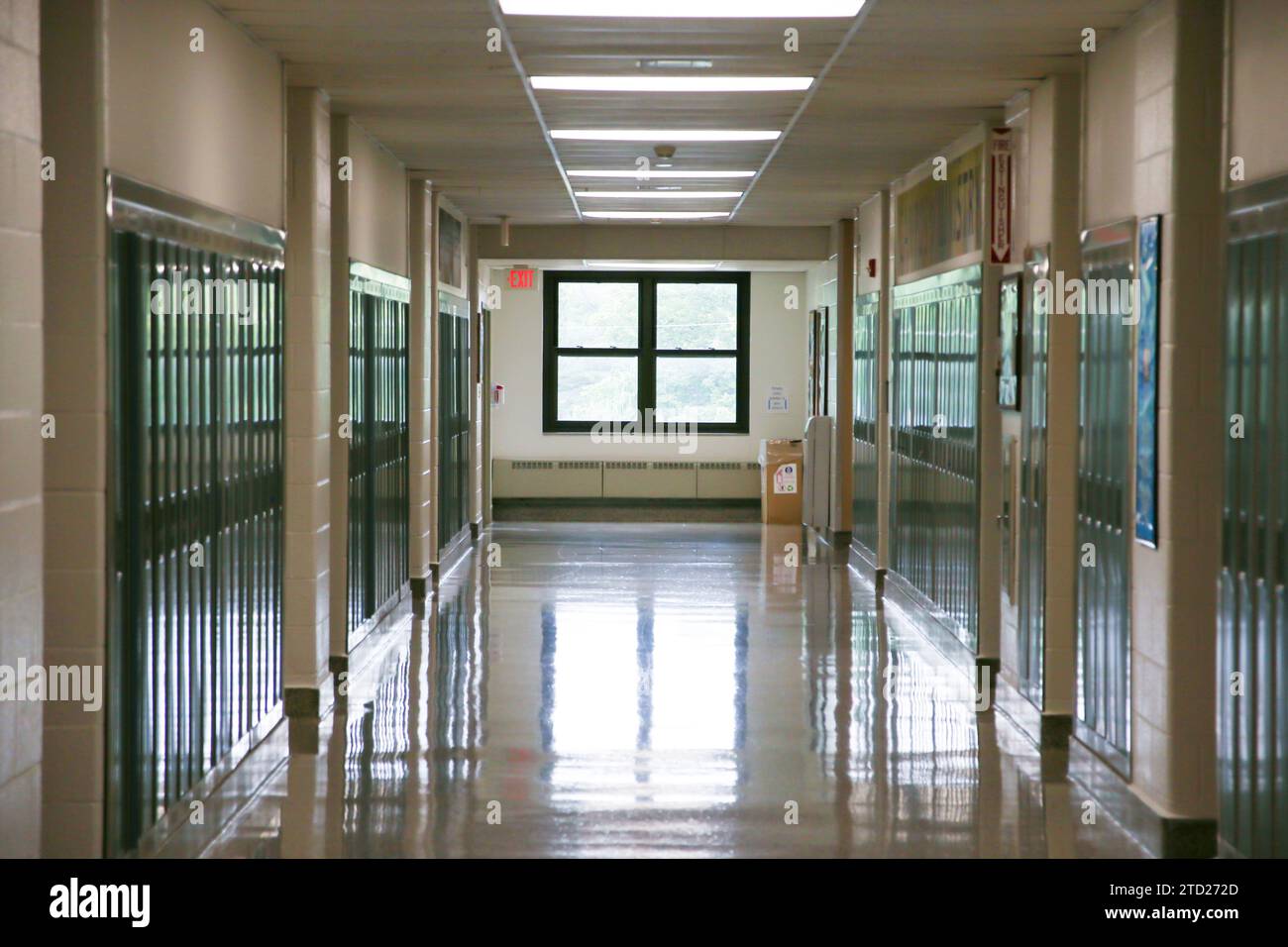Un lungo corridoio fiancheggiato da armadietti scolastici che conducono ad una finestra in un edificio delle scuole superiori. Foto Stock