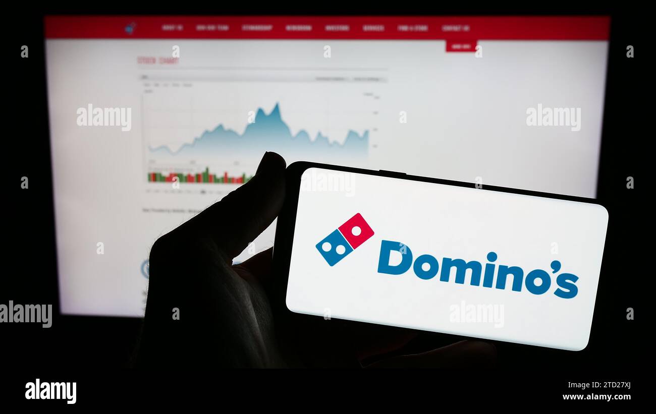 Persona che possiede un telefono cellulare con il logo della catena di ristoranti americana Domino's Pizza Inc. Davanti alla pagina Web. Concentrarsi sul display del telefono. Foto Stock