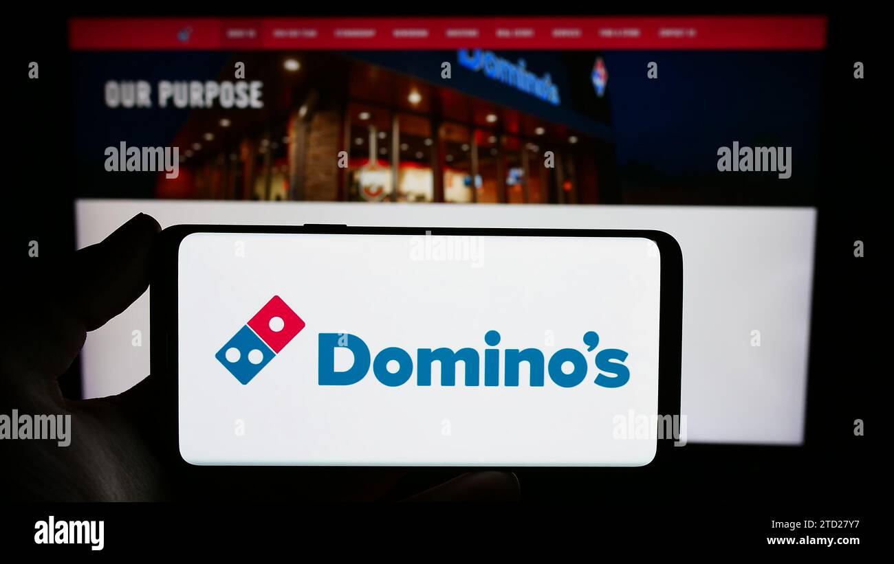 Persona che possiede il cellulare con il logo della catena di ristoranti statunitense Domino's Pizza Inc. Davanti alla pagina Web aziendale. Concentrarsi sul display del telefono. Foto Stock
