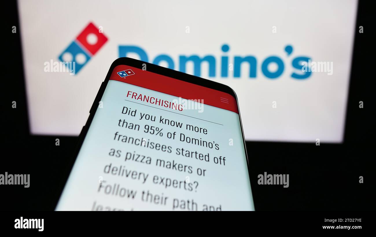 Telefono cellulare con sito Web della catena di ristoranti statunitense Domino's Pizza Inc. Davanti al logo aziendale. Mettere a fuoco in alto a sinistra sul display del telefono. Foto Stock