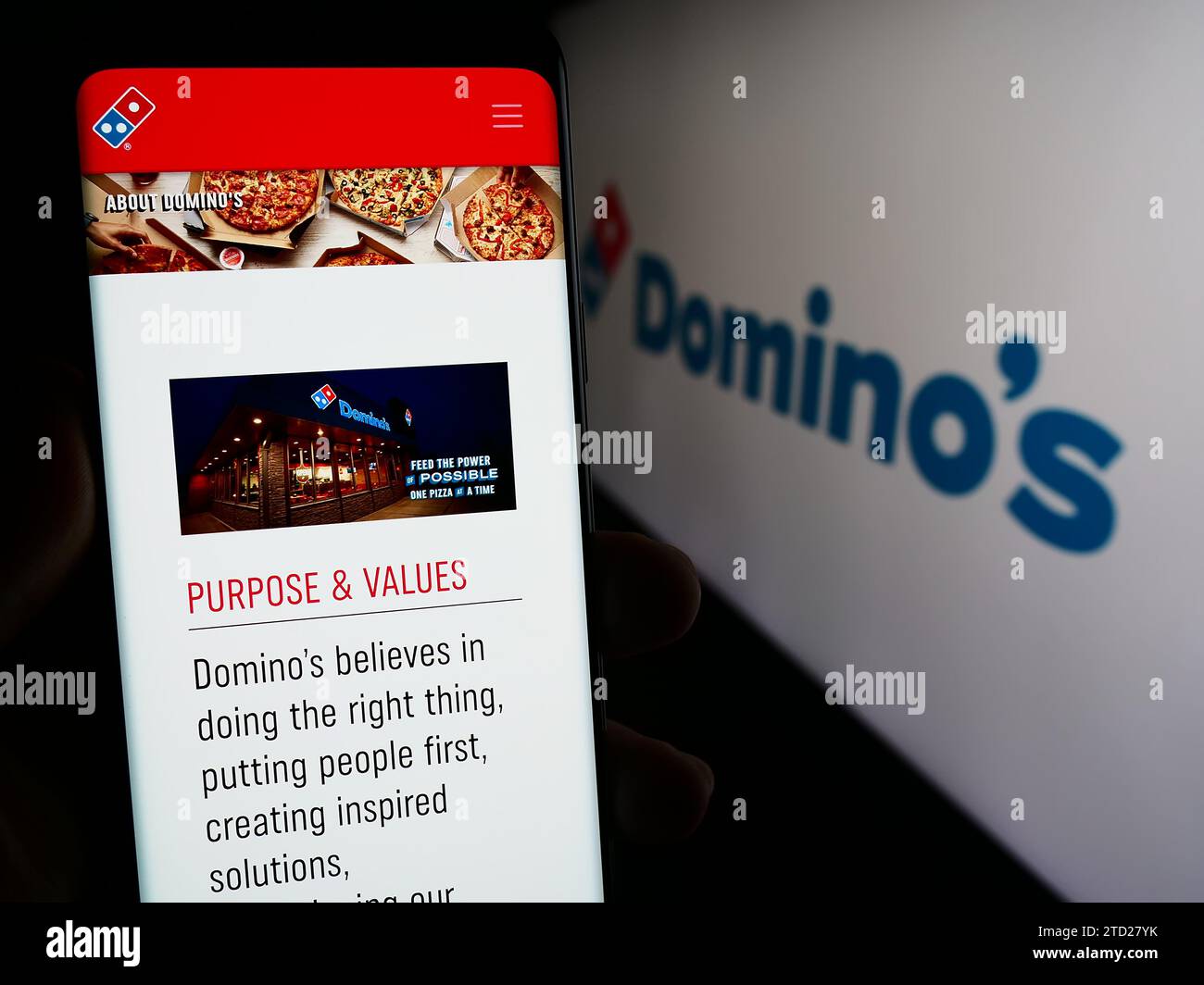 Persona che possiede uno smartphone con una pagina Web della catena di ristoranti statunitense Domino's Pizza Inc. Davanti al logo. Concentrarsi sul centro del display del telefono. Foto Stock