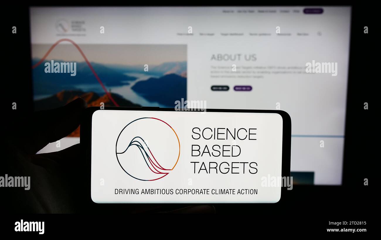 Persona che possiede uno smartphone con il logo dell'organizzazione Science Based Targets Initiative (SBTi) davanti al sito Web. Concentrarsi sul display del telefono. Foto Stock