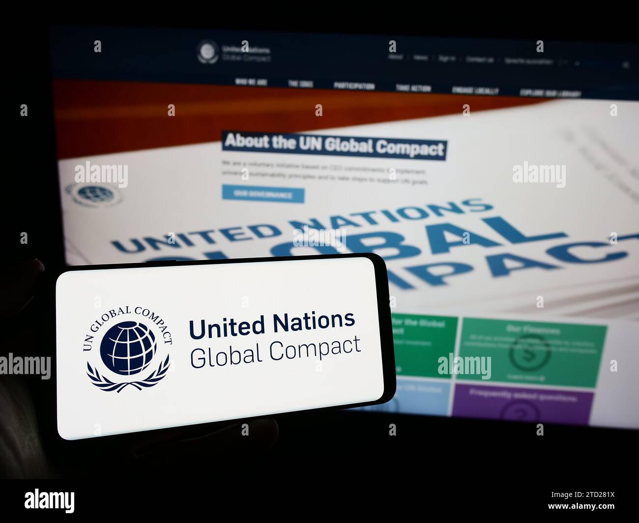 Persona in possesso di un telefono cellulare con il logo del patto ONU Global Compact delle Nazioni Unite davanti alla pagina Web. Concentrarsi sul display del telefono. Foto Stock