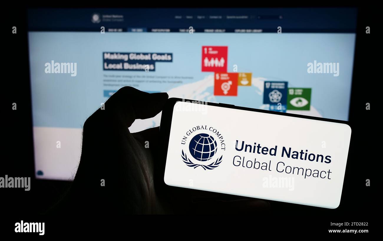 Persona che possiede uno smartphone con il logo del Patto delle Nazioni Unite Global Compact davanti al sito Web. Concentrarsi sul display del telefono. Foto Stock