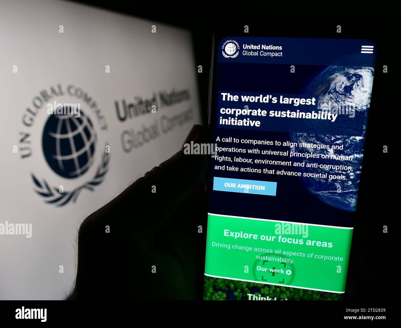 Persona in possesso di cellulare con pagina Web del Patto delle Nazioni Unite Global Compact davanti al logo. Concentrarsi sul centro del display del telefono. Foto Stock
