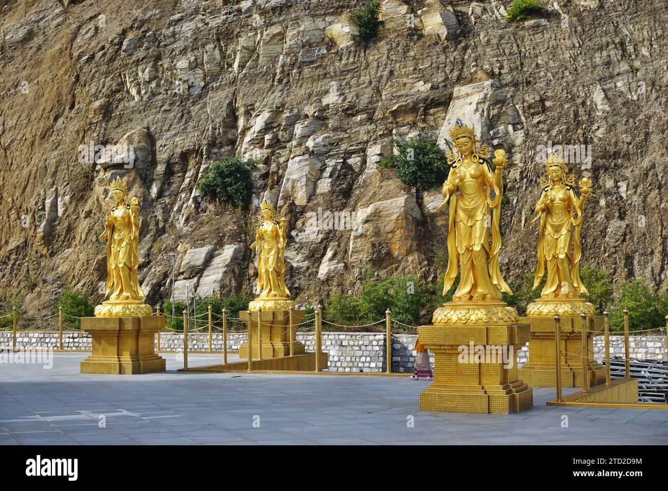 Le statue delle dee d'oro contrastano con la parete rocciosa ruvida dietro al monumento Buddha Dordenma nel parco naturale Kuensel Phodrang vicino a Thimphu, Bhutan. Foto Stock