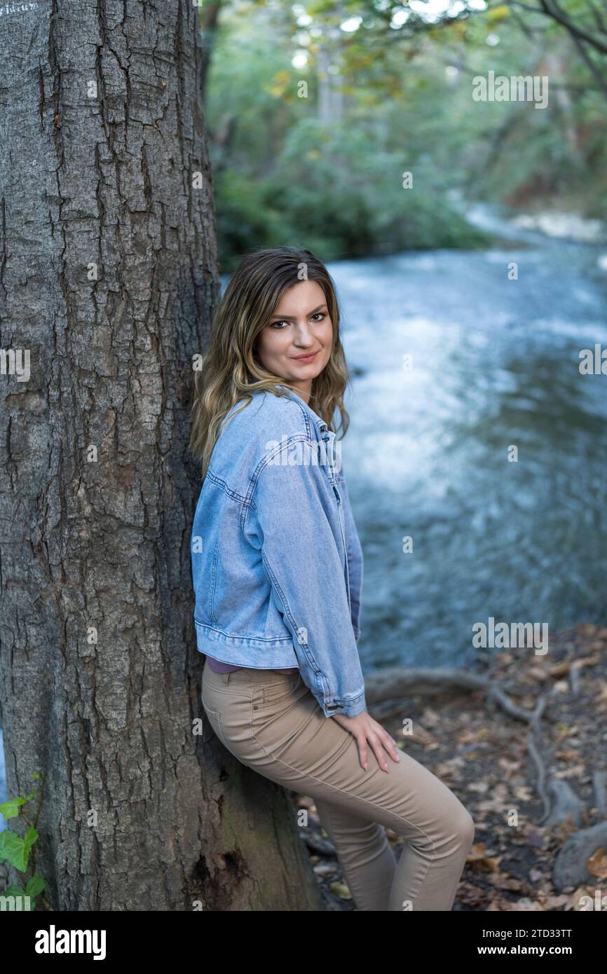 Attraente giovane donna che indossa una giacca in denim dai colori pastello che si appoggia al sentiero escursionistico Tree Creek Foto Stock