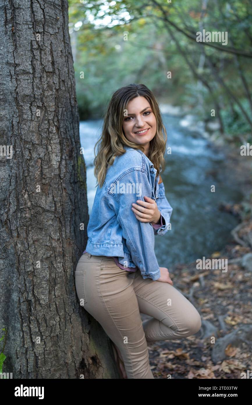 Attraente giovane donna che indossa una giacca in denim dai colori pastello che si appoggia al sentiero escursionistico Tree Creek Foto Stock