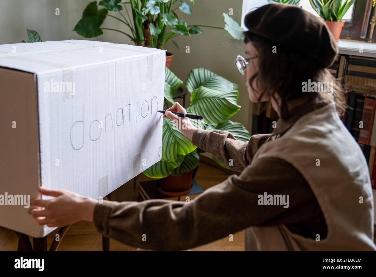 Ragazza interessata studentessa altruista volontaria che prepara la scatola per le donazioni scrivendo iscrizioni a casa. Foto Stock