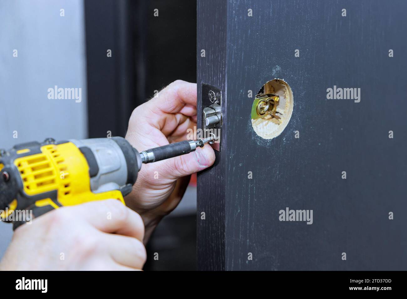 Con l'aiuto di un cacciavite, il falegname installa le maniglie di blocco nella porta della camera Foto Stock