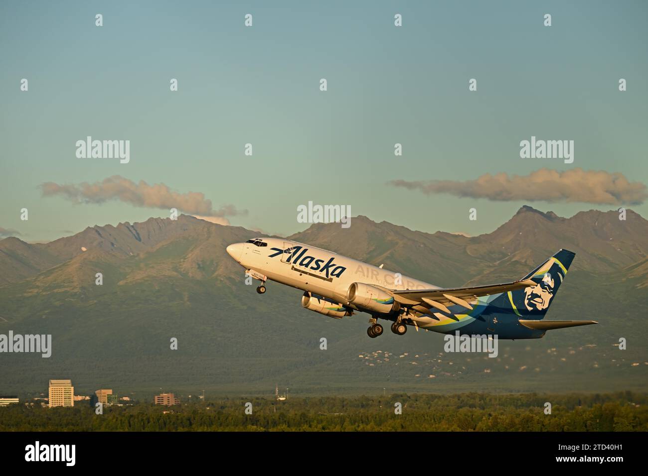 Sullo sfondo delle Chugach Mountains e delle case di Anchorage, un aereo cargo Alaska Airlines decolla dalla Ted Stevens International Foto Stock