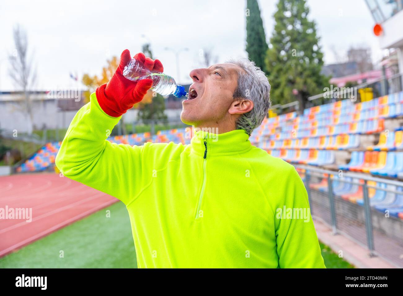 Uomo sportivo maturo che beve acqua dopo aver corso in pista in inverno Foto Stock