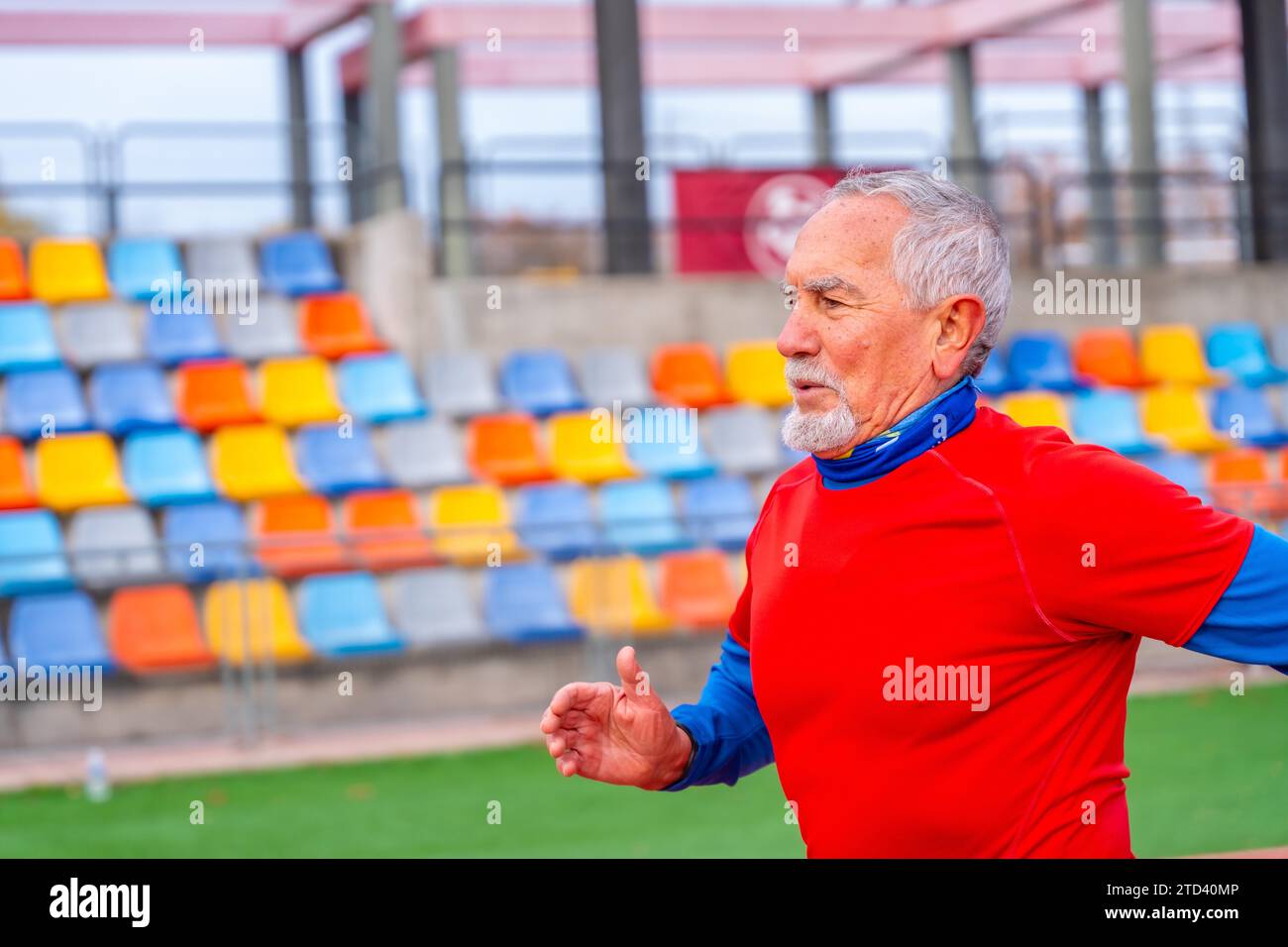 Foto con vista laterale con spazio fotocopie di un uomo anziano che corre in un campo sportivo all'aperto in inverno Foto Stock