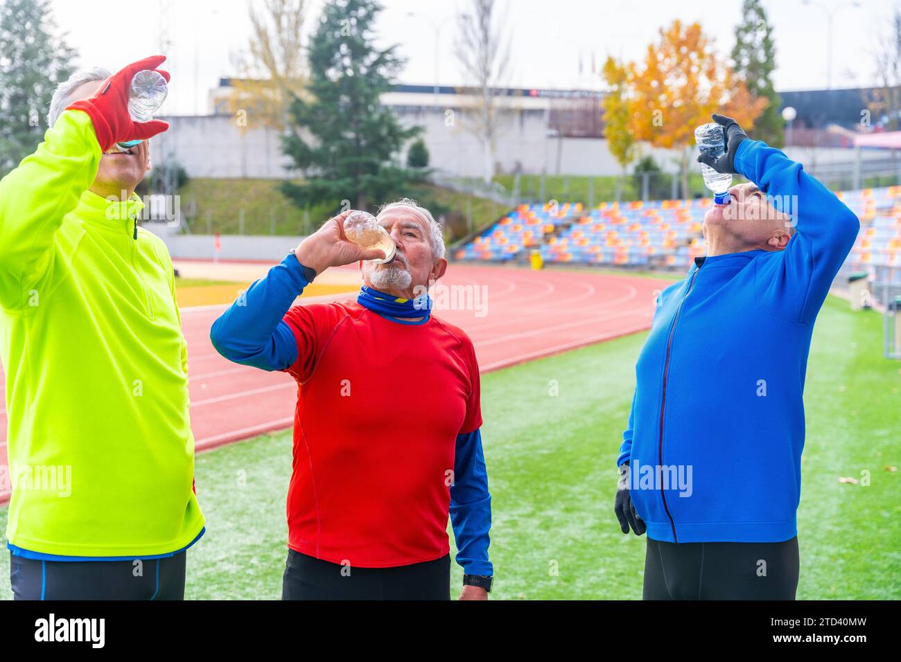 Uomini anziani che bevono acqua dopo aver corso lungo una pista atletica all'aperto in inverno Foto Stock