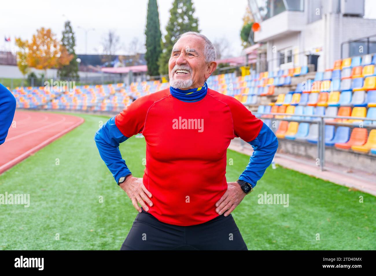 Anziano sorridente con abiti sportivi che si riscaldano in pista e in campo in inverno Foto Stock