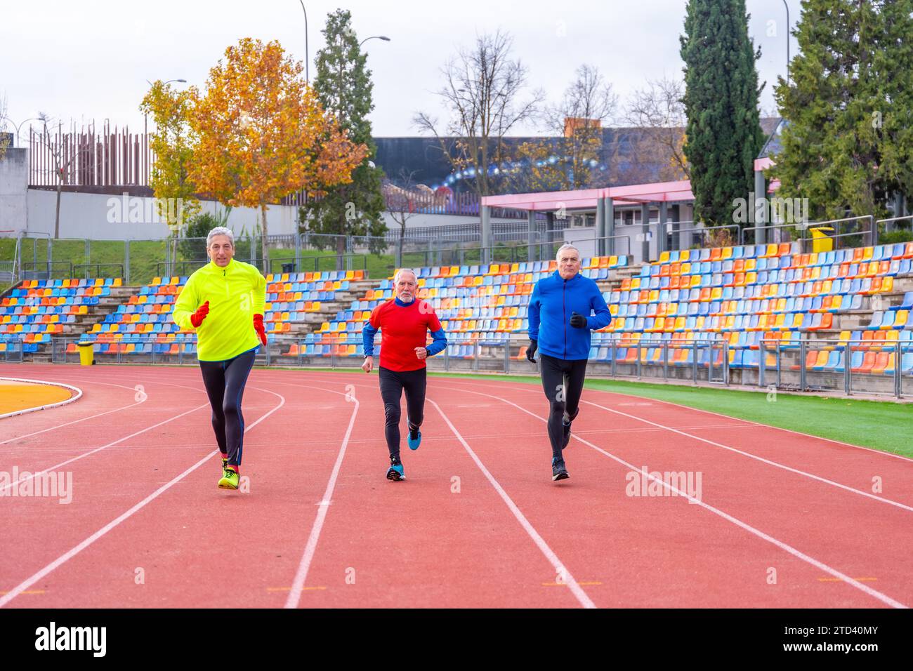 Vista frontale di tre uomini sportivi maturi che corrono in una pista di atletica Foto Stock