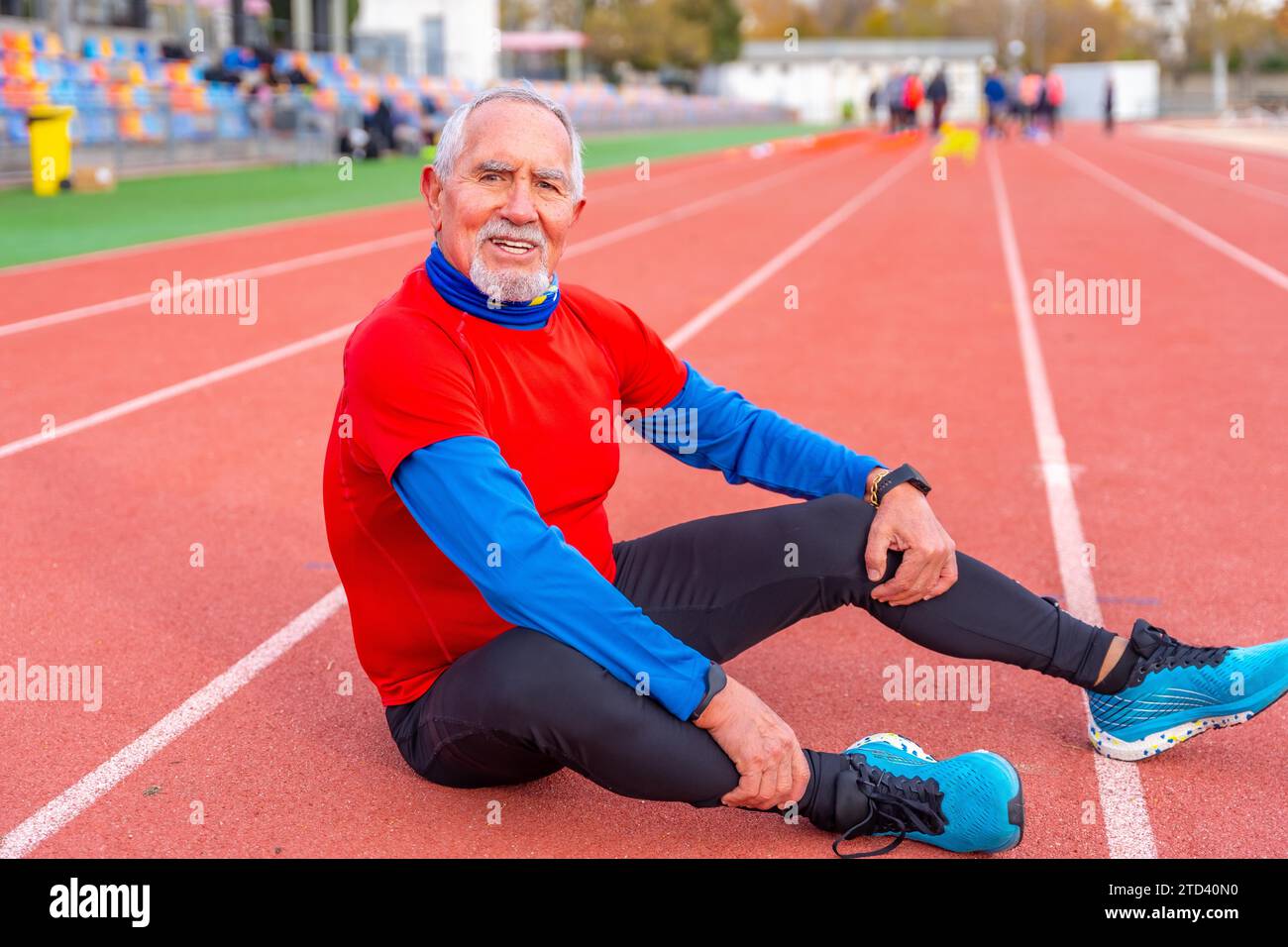 Ritratto di un vecchio sorridente e sportivo seduto stanco su una pista dopo aver corso Foto Stock