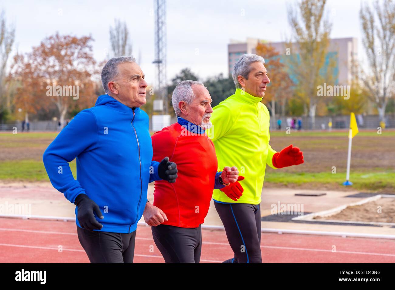 Uomini sportivi senior con abiti sportivi colorati che corrono insieme in un campo di atletica Foto Stock