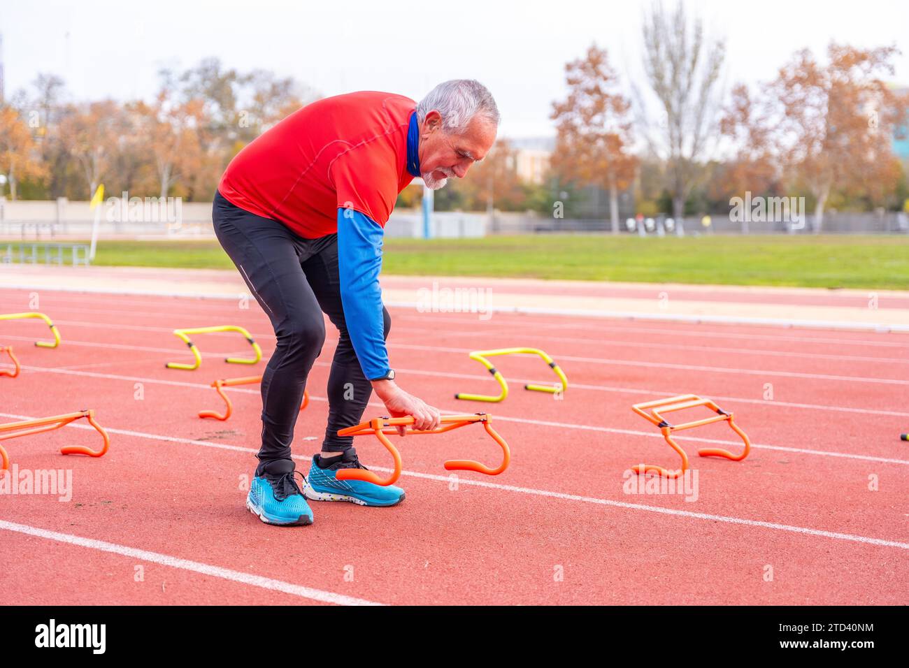 Uomo anziano sportivo che mette blocchi di partenza su una pista di atletica in inverno Foto Stock