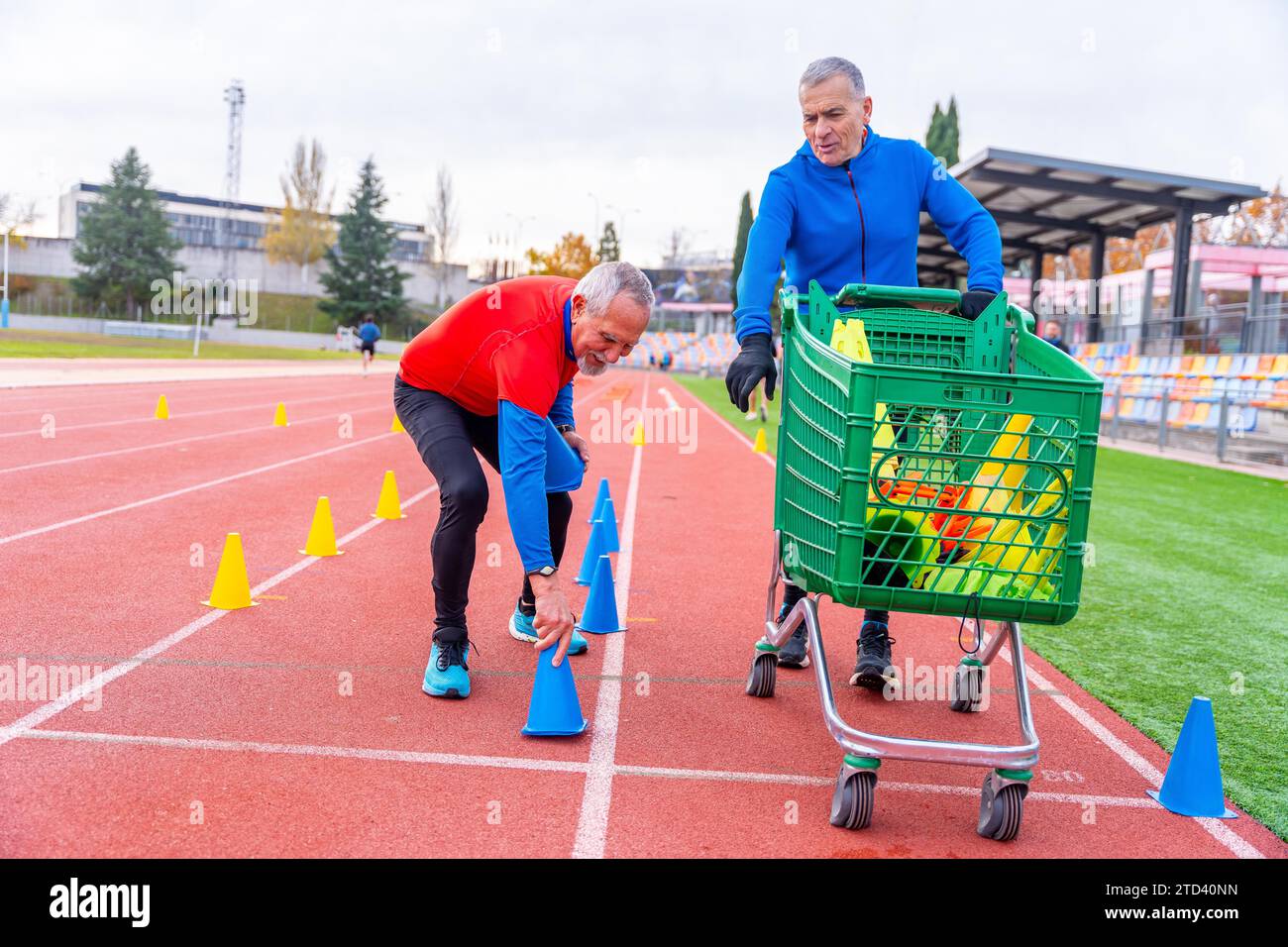 Uomini con un carrello che preparano coni per allenarsi in pista all'aperto in inverno Foto Stock