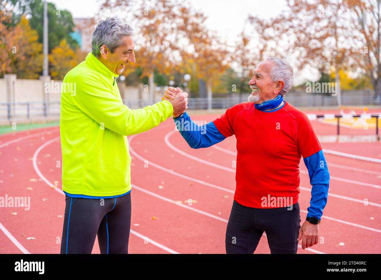 Amici sportivi anziani che si stringono la mano con orgoglio dopo aver corso in una pista all'aperto in inverno Foto Stock