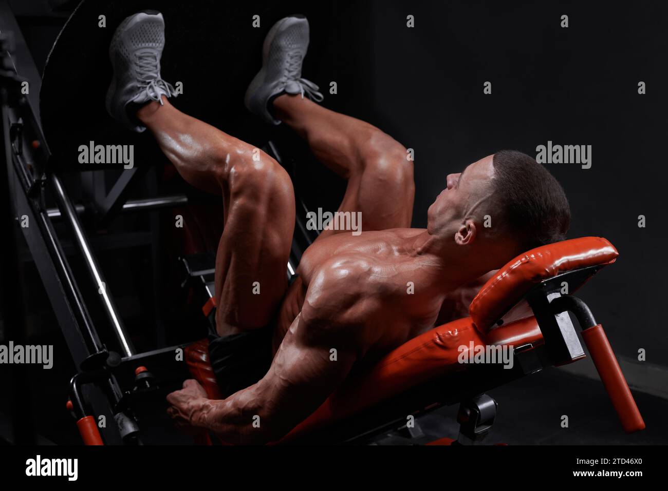 Vista laterale dell'atleta maschile etnico muscoloso sdraiato sulla pressa per gambe e muscoli che pompano durante l'allenamento in palestra. Supporti misti Foto Stock