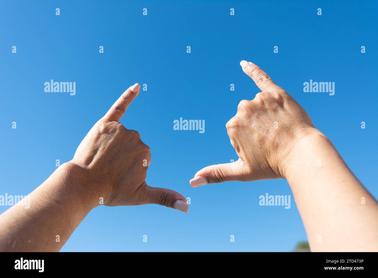 Le mani di una donna che mostra il segno del surfista sullo sfondo blu del cielo Foto Stock