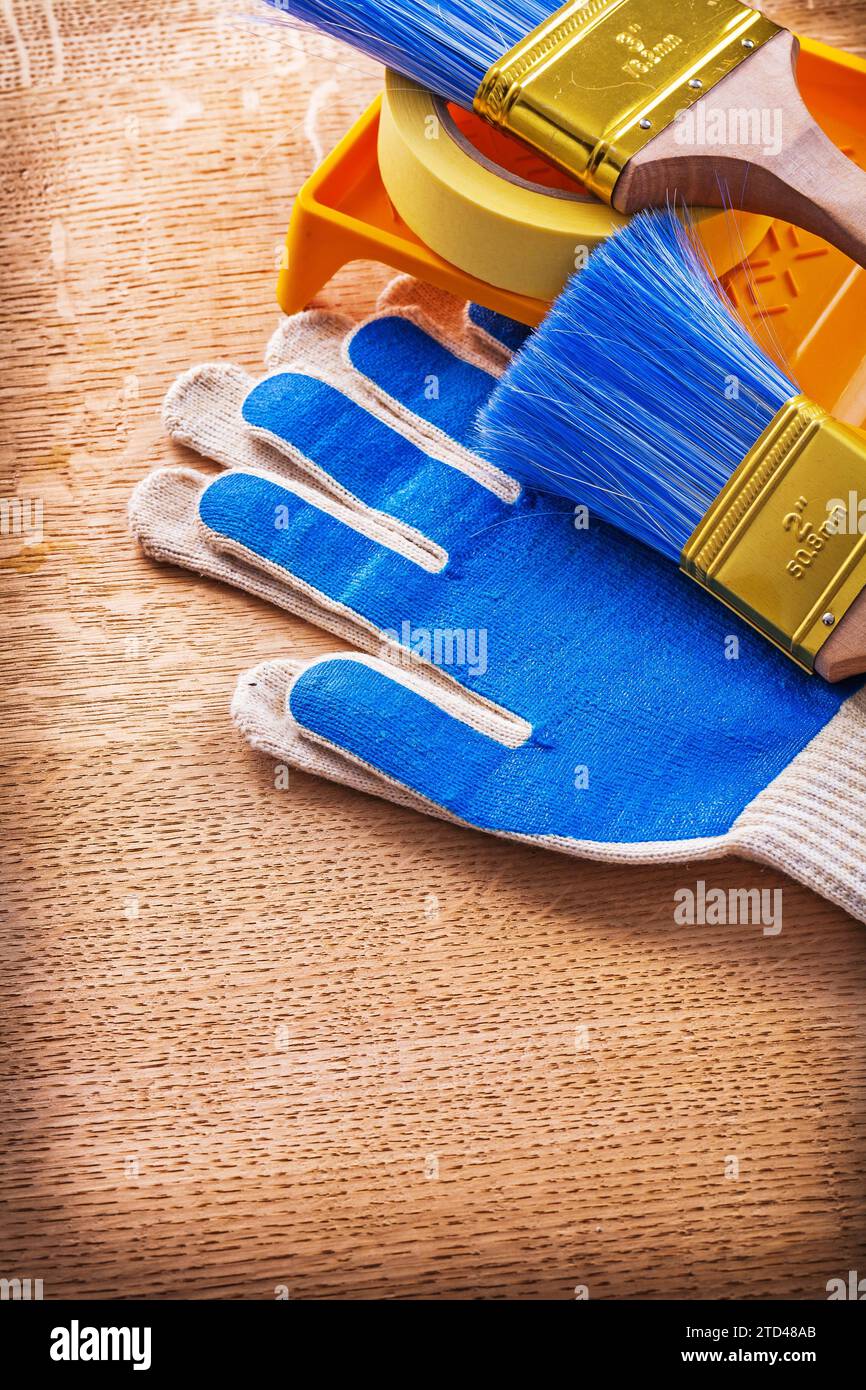 Vassoio di verniciatura spazzole nastro adesivo e guanti protettivi su pannello di legno concetto di costruzione Foto Stock