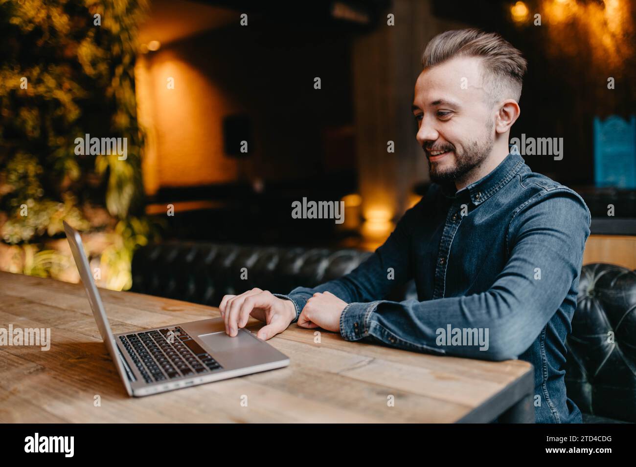 Giovane freelance sorridente di successo con una camicia in denim che lavora al computer portatile in covoking Foto Stock