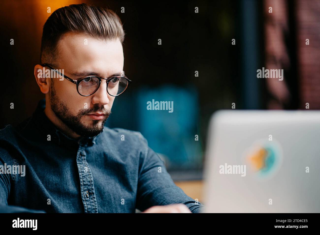 Giovane freelance di successo con una camicia in denim che lavora al computer portatile in covoking Foto Stock