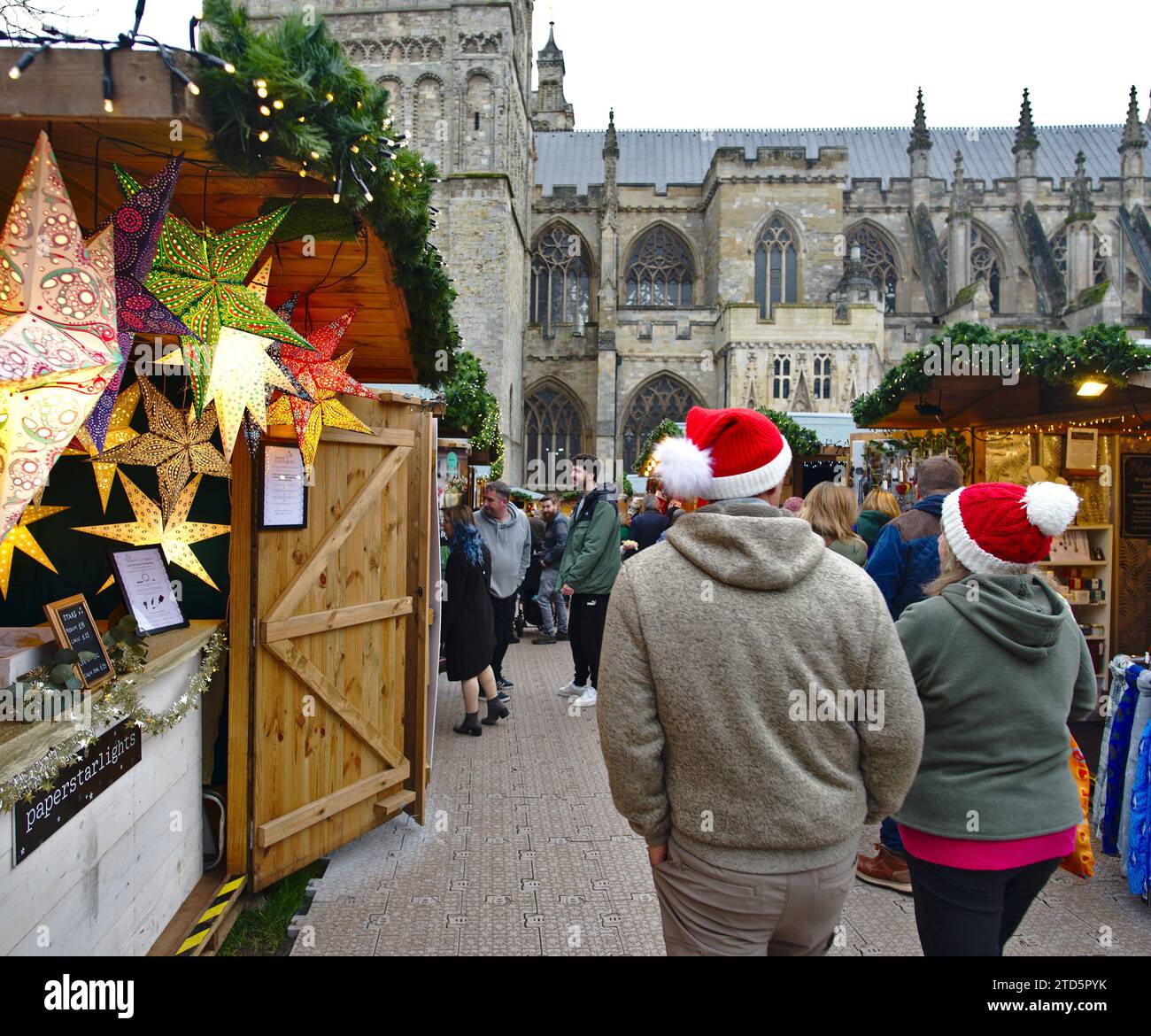 Le persone che indossano i cappelli di Babbo Natale camminano attraverso il mercato di Natale sulla Exeter Cathedral Green. Exeter, Devon, Regno Unito Foto Stock